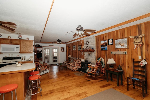 kitchen with white appliances, wooden walls, light hardwood / wood-style floors, and a breakfast bar area