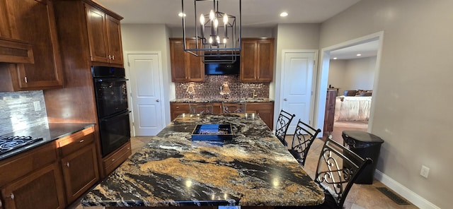 kitchen featuring black double oven, a center island, backsplash, and dark stone counters