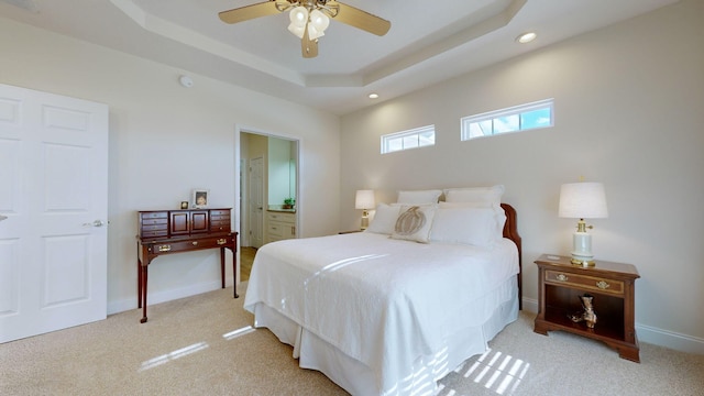 bedroom with ceiling fan, light colored carpet, a tray ceiling, and ensuite bath