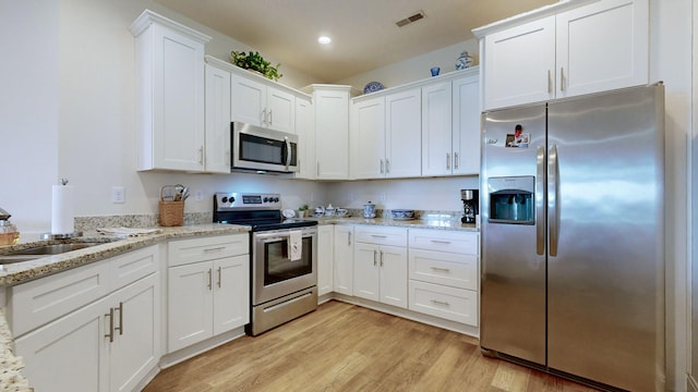 kitchen with white cabinetry, light stone countertops, light hardwood / wood-style flooring, and stainless steel appliances