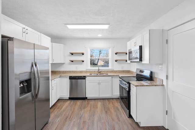 kitchen with sink, light wood-type flooring, white cabinets, stainless steel appliances, and a textured ceiling