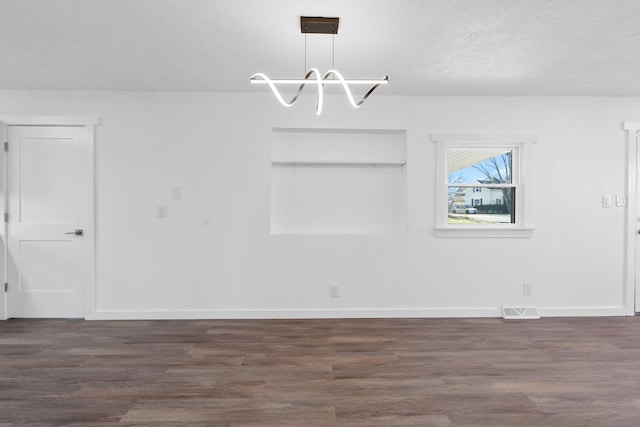 unfurnished dining area with an inviting chandelier, a textured ceiling, and dark hardwood / wood-style flooring