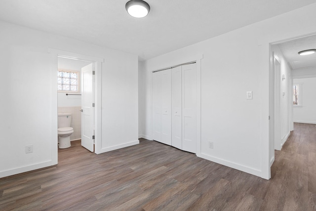 unfurnished bedroom with ensuite bathroom, dark hardwood / wood-style flooring, and a closet