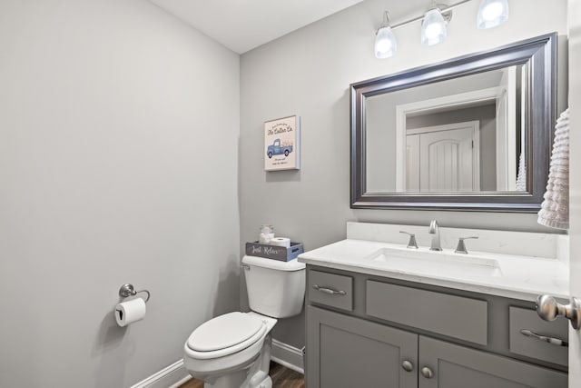 half bathroom featuring toilet, baseboards, wood finished floors, and vanity