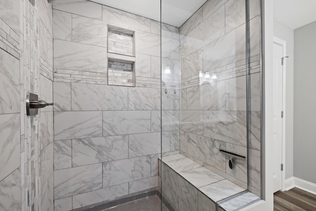 full bath with a tile shower, baseboards, and wood finished floors