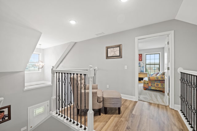 hall featuring light wood finished floors, baseboards, vaulted ceiling, an upstairs landing, and a notable chandelier