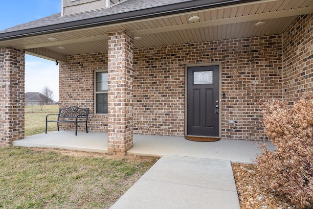 entrance to property featuring a patio area, roof with shingles, and brick siding