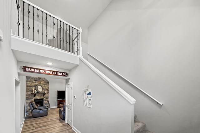 staircase featuring a stone fireplace, wood finished floors, and a high ceiling