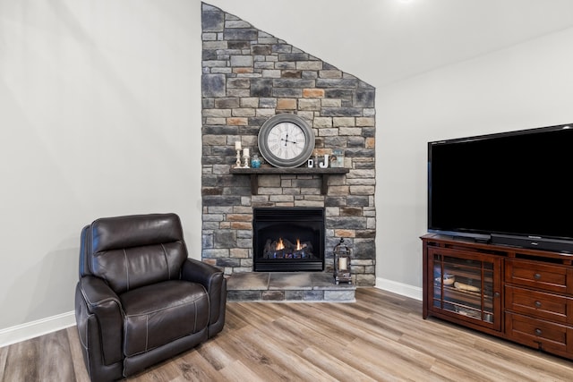 living room featuring lofted ceiling, baseboards, a stone fireplace, and light wood finished floors