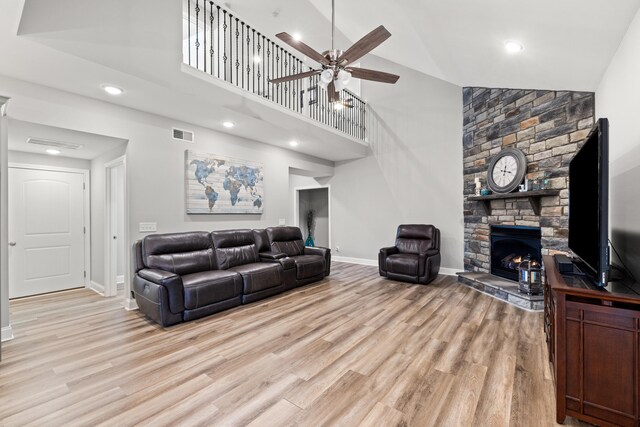 living area featuring a fireplace, visible vents, light wood-style flooring, high vaulted ceiling, and baseboards