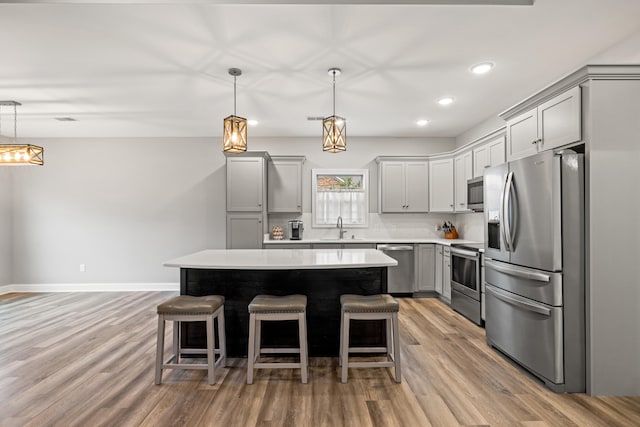 kitchen featuring stainless steel appliances, light countertops, a kitchen island, and hanging light fixtures