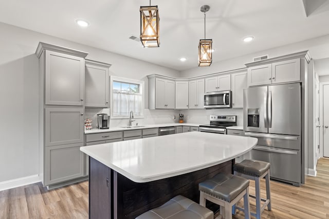 kitchen with stainless steel appliances, a kitchen island, a sink, hanging light fixtures, and light countertops