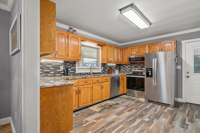 kitchen with crown molding, appliances with stainless steel finishes, light stone countertops, and light hardwood / wood-style flooring