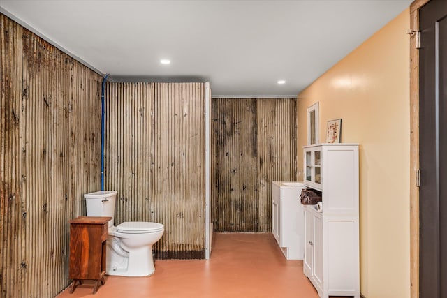 bathroom with wooden walls, toilet, and concrete flooring