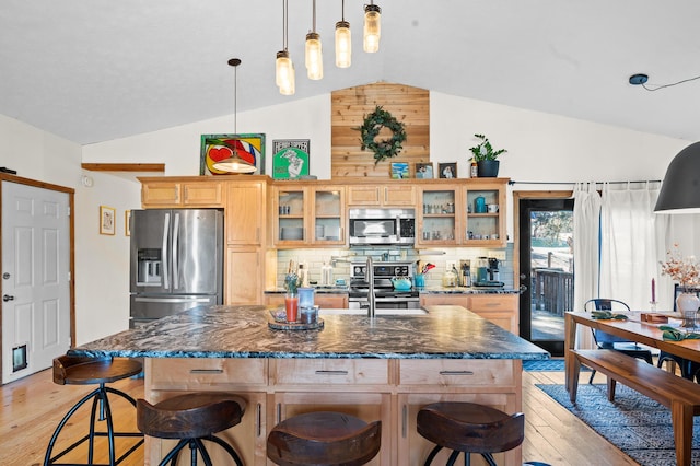 kitchen featuring appliances with stainless steel finishes, a kitchen island with sink, dark stone countertops, light hardwood / wood-style floors, and vaulted ceiling