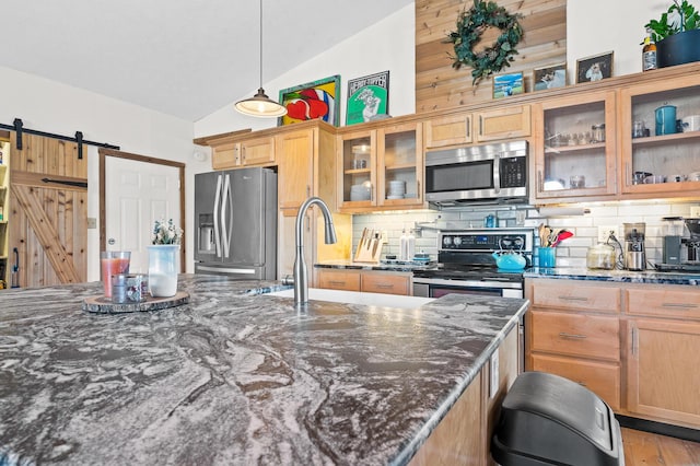 kitchen with appliances with stainless steel finishes, decorative backsplash, hanging light fixtures, dark stone counters, and a barn door