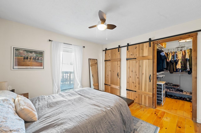 bedroom with wood-type flooring, a textured ceiling, a barn door, a walk in closet, and a closet