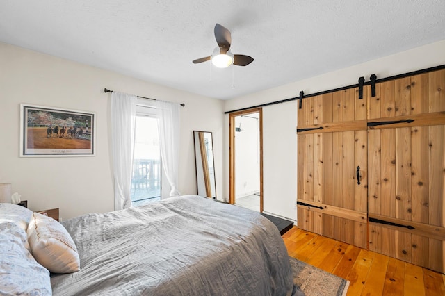 bedroom featuring ceiling fan, hardwood / wood-style flooring, a barn door, and a textured ceiling