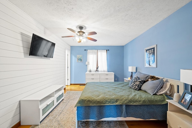 bedroom featuring ceiling fan, wooden walls, a textured ceiling, and light wood-type flooring