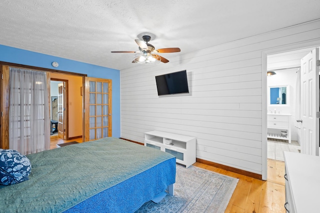 bedroom featuring french doors, wood walls, light hardwood / wood-style flooring, and a textured ceiling