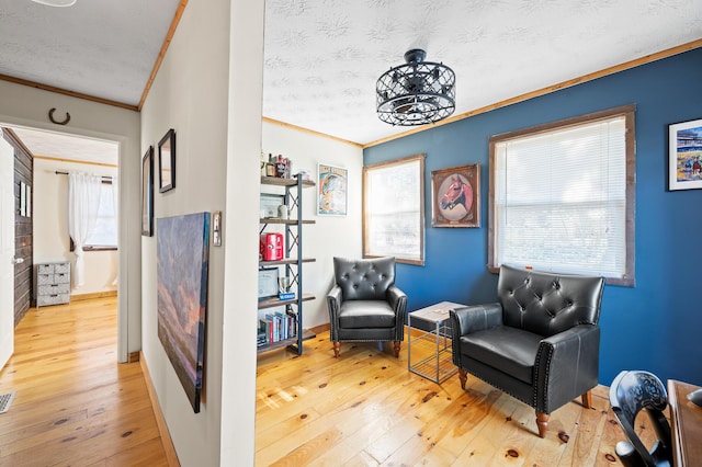 living area with light hardwood / wood-style flooring, ornamental molding, and a textured ceiling