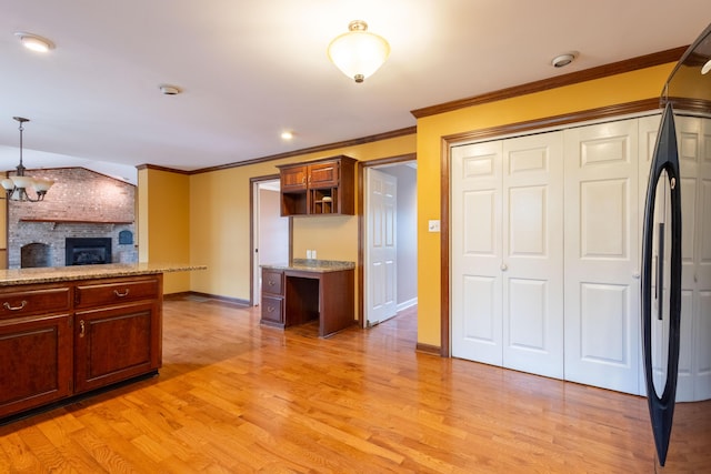 kitchen with light hardwood / wood-style flooring, black refrigerator, ornamental molding, a brick fireplace, and decorative light fixtures