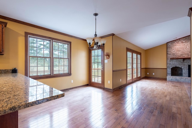 unfurnished living room with lofted ceiling, a notable chandelier, wood-type flooring, ornamental molding, and a brick fireplace