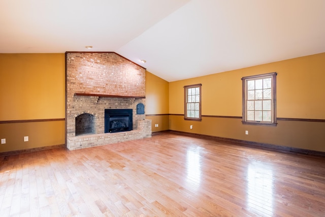 unfurnished living room featuring hardwood / wood-style flooring, lofted ceiling, and a brick fireplace