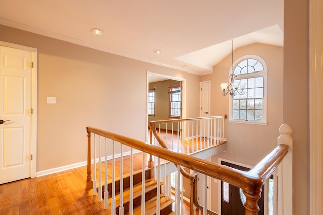 hallway with lofted ceiling, ornamental molding, light hardwood / wood-style floors, and an inviting chandelier