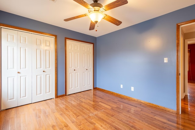 unfurnished bedroom with two closets, light hardwood / wood-style floors, and ceiling fan