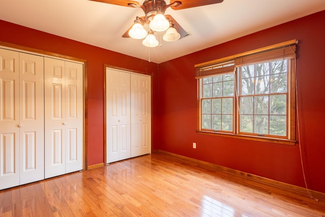 unfurnished bedroom featuring ceiling fan, two closets, and light hardwood / wood-style floors