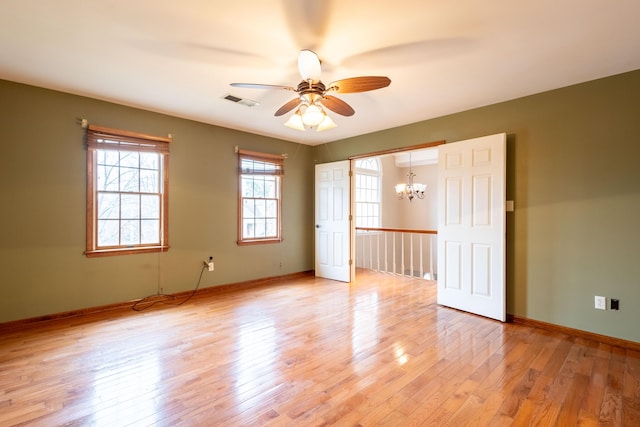 empty room featuring ceiling fan with notable chandelier and light wood-type flooring