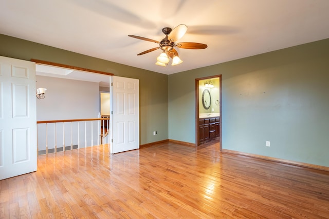 empty room featuring ceiling fan with notable chandelier and light wood-type flooring