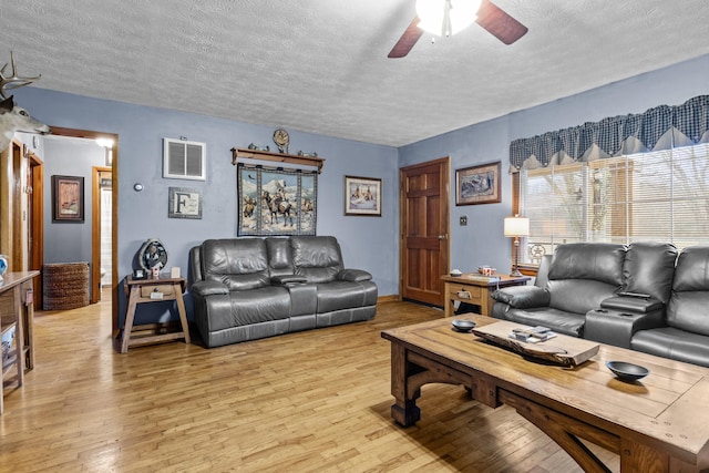 living room featuring ceiling fan, light hardwood / wood-style flooring, and a textured ceiling