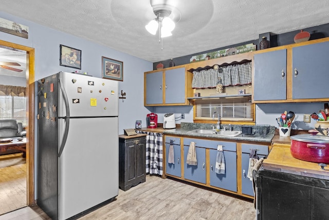 kitchen featuring sink, light hardwood / wood-style flooring, a textured ceiling, stainless steel refrigerator, and ceiling fan