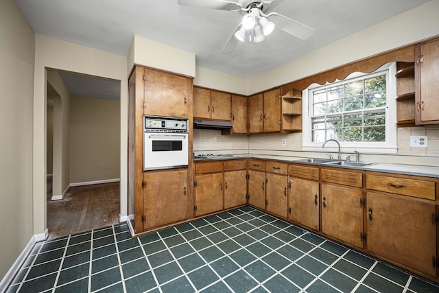 kitchen featuring sink, gas cooktop, ceiling fan, white oven, and decorative backsplash