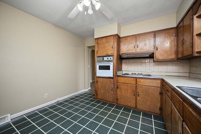 kitchen with sink, white oven, ceiling fan, stainless steel gas stovetop, and decorative backsplash