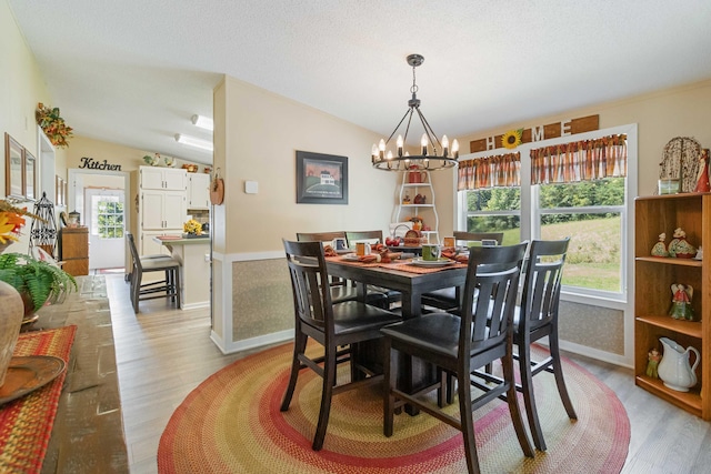 dining room with vaulted ceiling, a textured ceiling, a notable chandelier, and light hardwood / wood-style floors