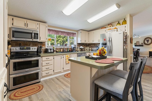 kitchen featuring a kitchen island, appliances with stainless steel finishes, sink, a kitchen bar, and light hardwood / wood-style floors