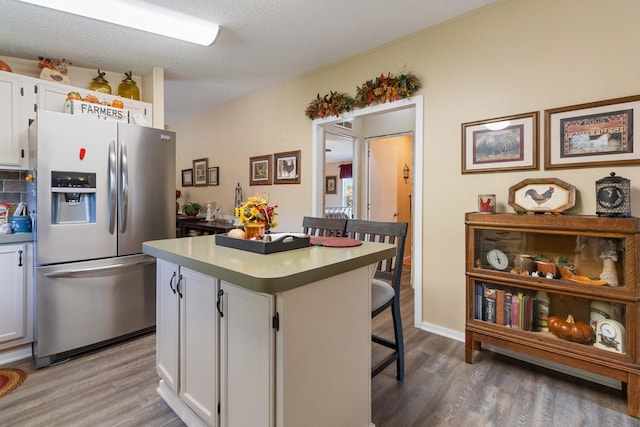 kitchen with a breakfast bar, stainless steel refrigerator with ice dispenser, wood-type flooring, white cabinets, and a kitchen island