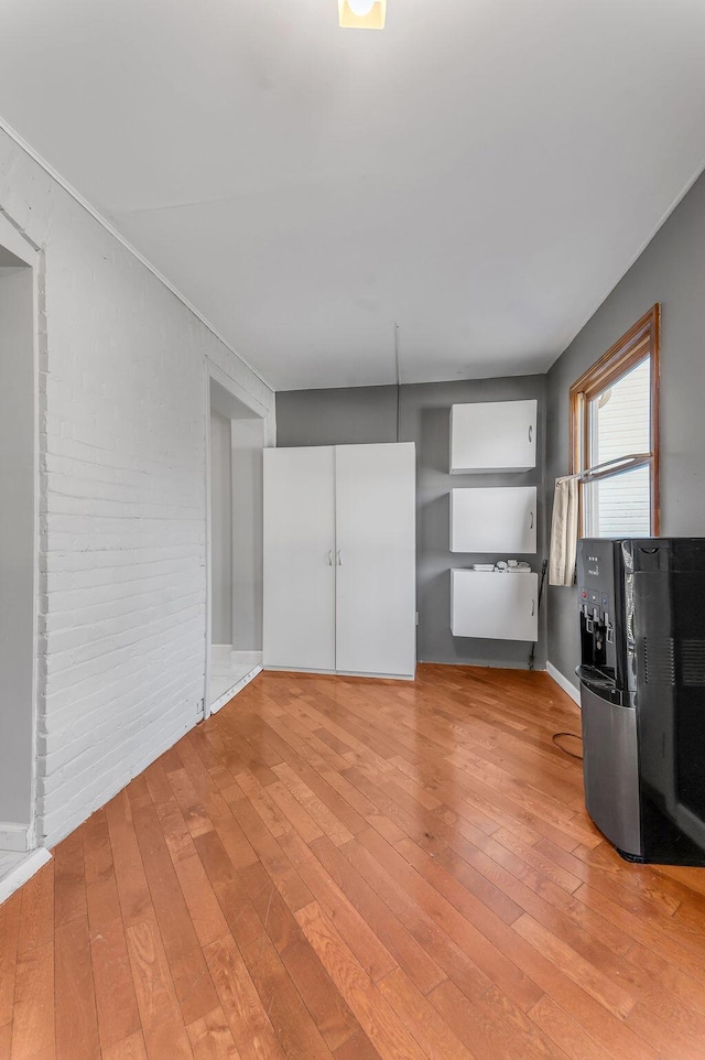 unfurnished bedroom with hardwood / wood-style floors and brick wall