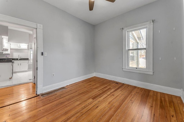 empty room with sink, ceiling fan, and light wood-type flooring