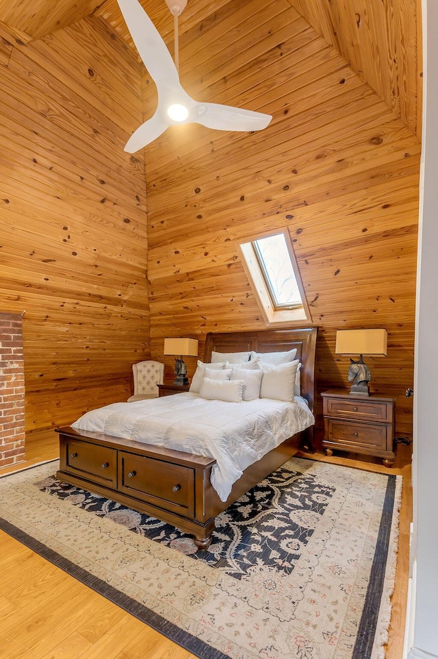 bedroom featuring wood walls, wood-type flooring, a skylight, a towering ceiling, and ceiling fan