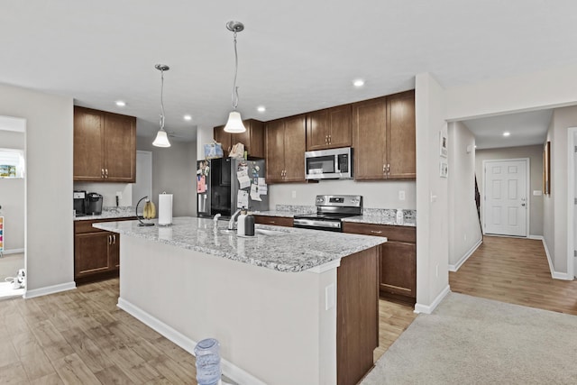 kitchen with sink, hanging light fixtures, a center island with sink, light hardwood / wood-style flooring, and appliances with stainless steel finishes