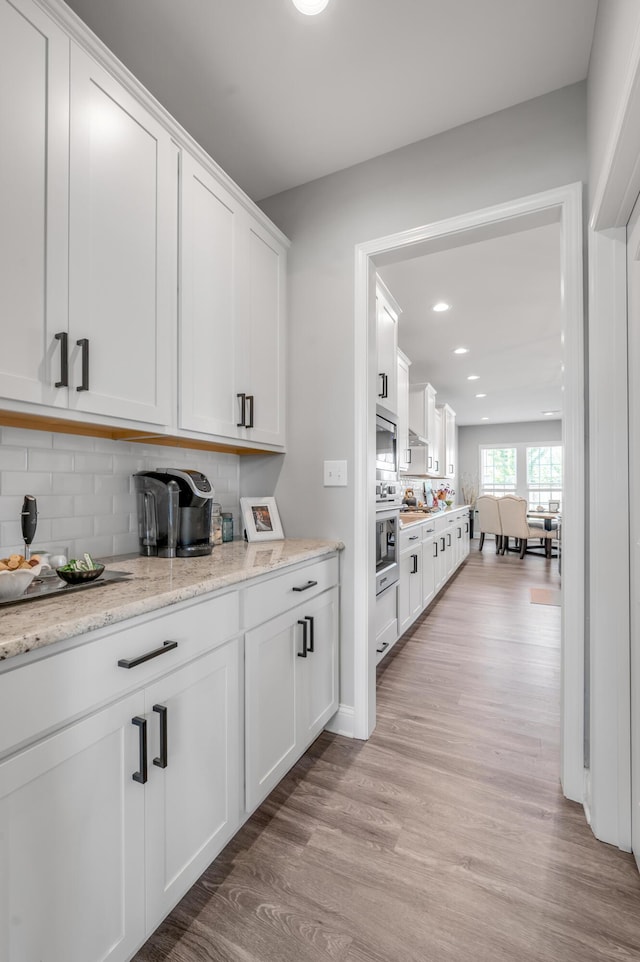 kitchen with backsplash, white cabinets, light stone counters, and light hardwood / wood-style floors