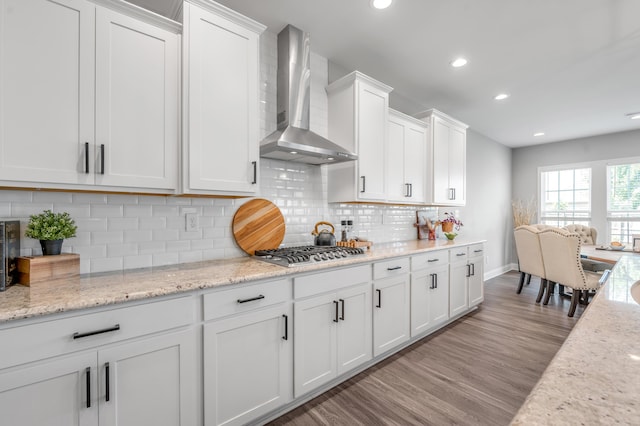 kitchen with stainless steel gas stovetop, tasteful backsplash, white cabinets, light hardwood / wood-style floors, and wall chimney exhaust hood