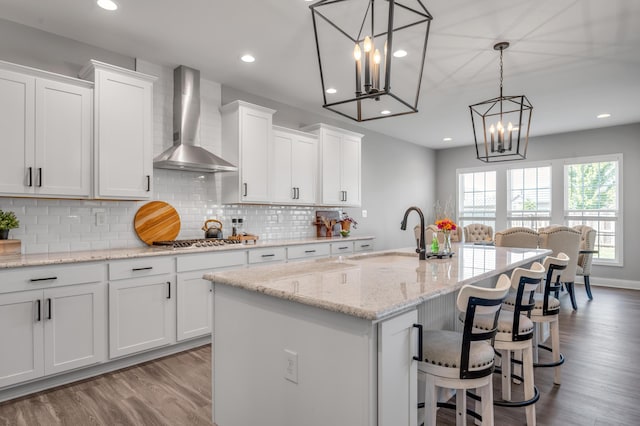 kitchen with wall chimney exhaust hood, sink, a kitchen island with sink, and white cabinets