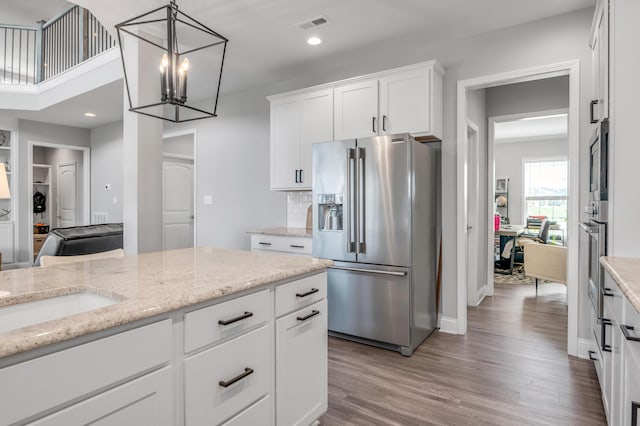 kitchen with appliances with stainless steel finishes, hardwood / wood-style floors, white cabinets, hanging light fixtures, and light stone counters