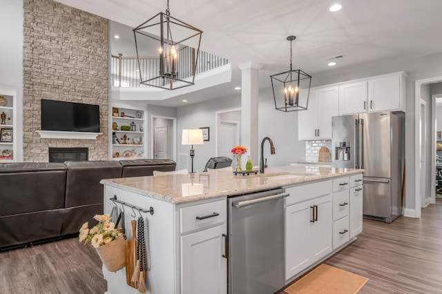 kitchen featuring stainless steel appliances, white cabinetry, an island with sink, and an inviting chandelier