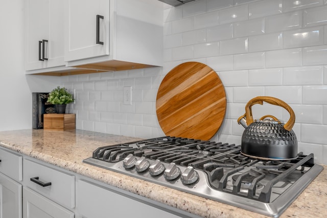 room details with decorative backsplash, light stone countertops, stainless steel gas cooktop, and white cabinets